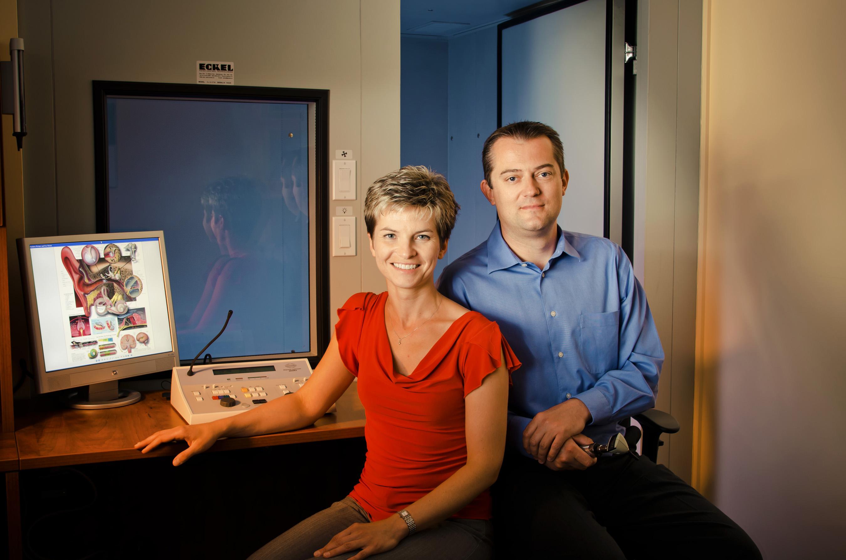 Female and male audiologists sitting at a hearing clinic desk.